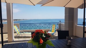 A terrace with a view of the sea, featuring two sun loungers and a table with a vase of flowers.