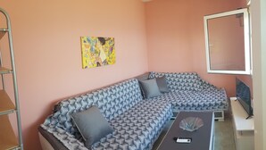 A modern living room with a blue patterned sofa, a glass coffee table, and a painting on the wall.