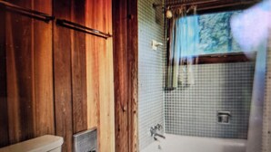 Un baño con paredes de madera, un inodoro y una bañera con zona de ducha.
