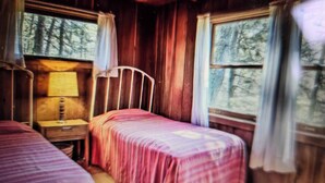 Habitación tipo cabaña con dos camas, una mesita de noche, una lámpara y cortinas.