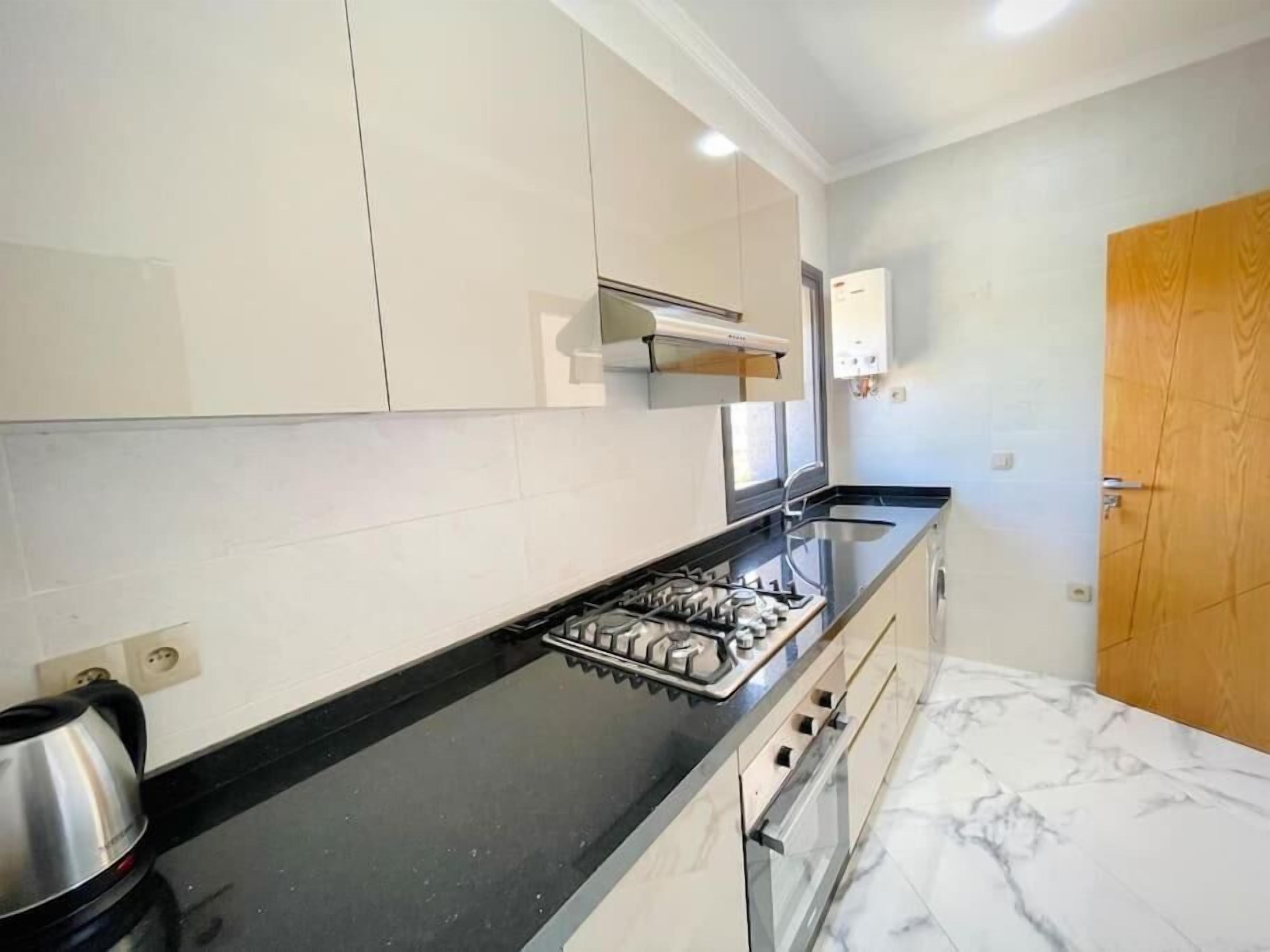 Une cuisine moderne avec des meubles blancs, un plan de travail noir, une cuisinière à gaz et un four encastré.