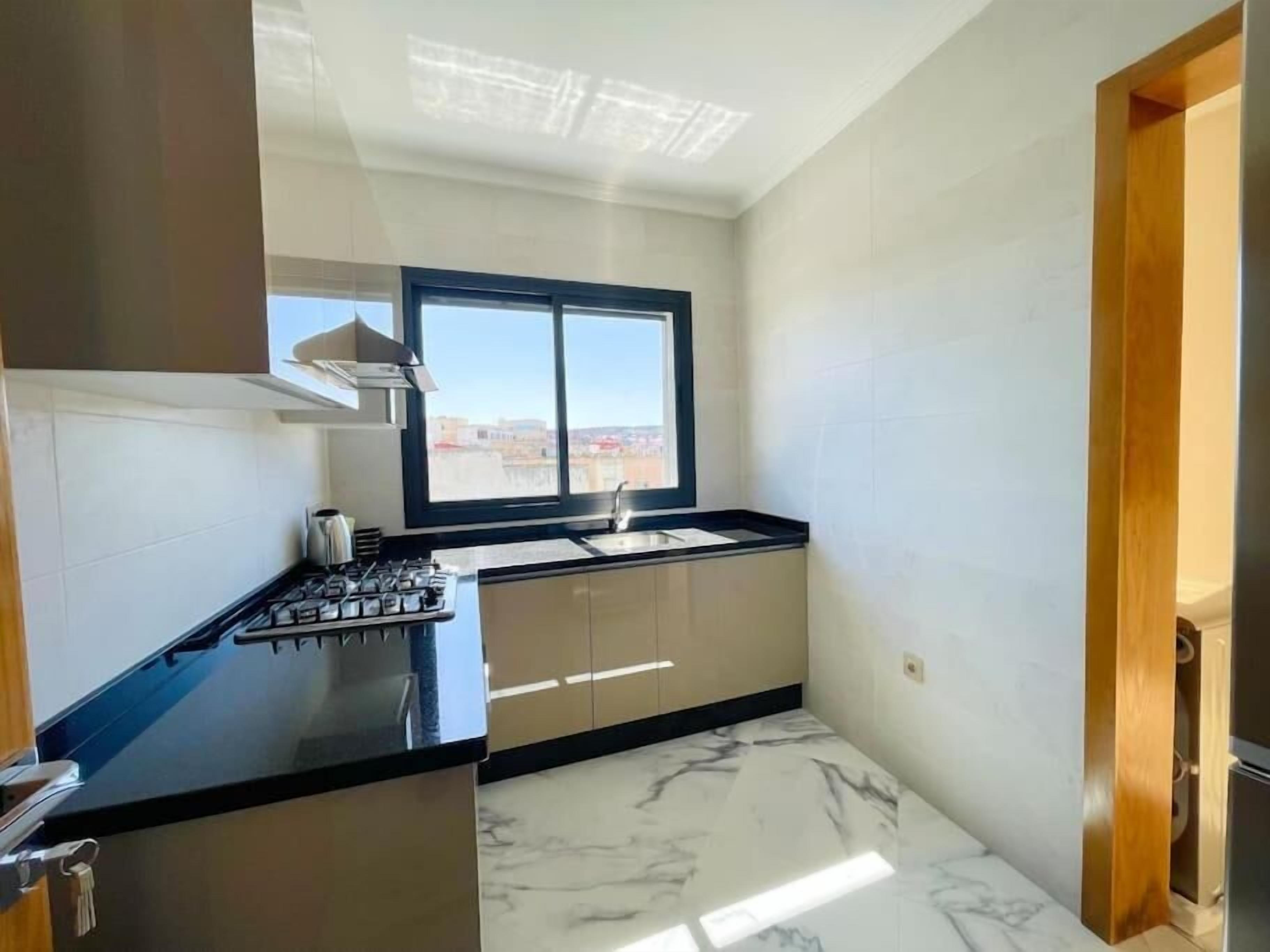 A compact kitchen with a gas stove, a window with a view, and a marble floor.