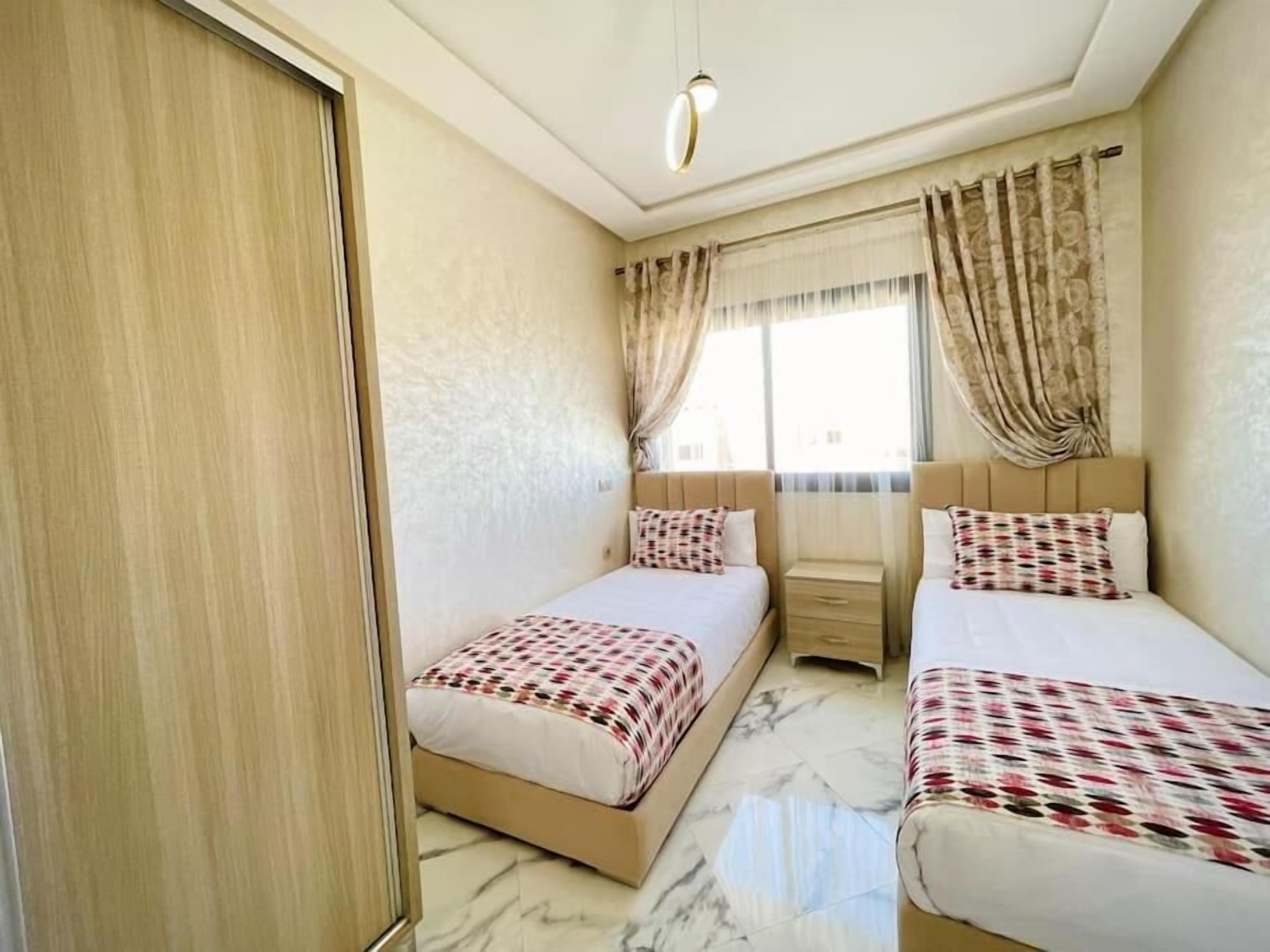 Habitación de hotel con dos camas, un armario de madera, una ventana con cortinas y piso de mármol.