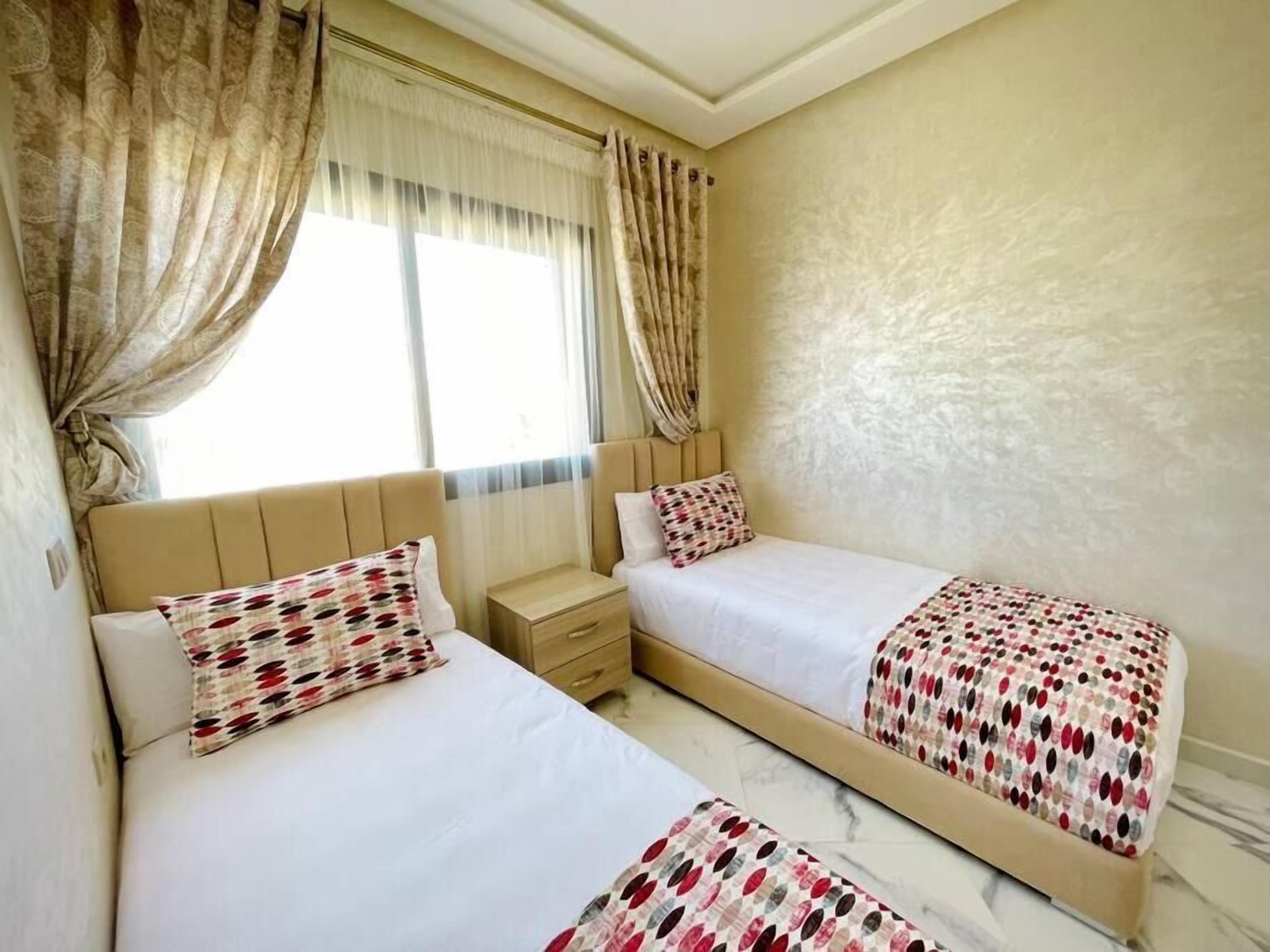 Una habitación de hotel con dos camas, una mesita de noche y una ventana con cortinas.