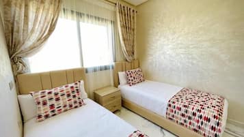 A hotel room with two beds, a nightstand, and a window with curtains.