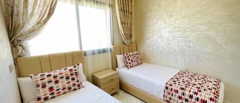 A hotel room with two beds, a nightstand, and a window with curtains.