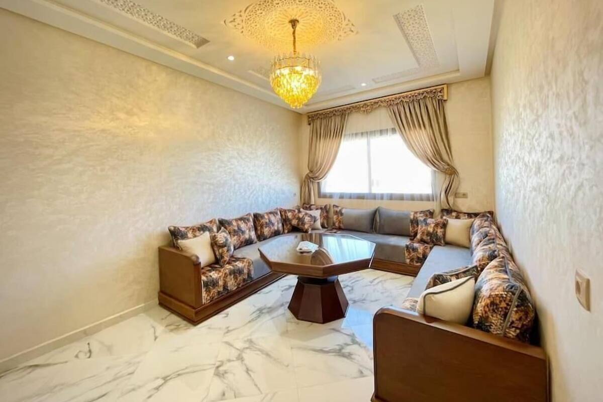 A spacious living room with a large sectional sofa, a glass coffee table, and a chandelier.