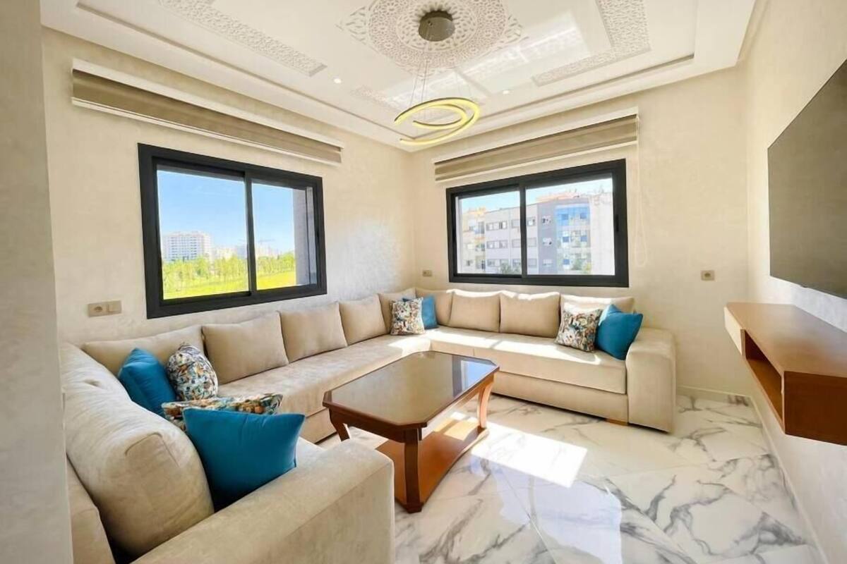 A modern living room with a sectional sofa, a marble coffee table, and large windows offering a city view.