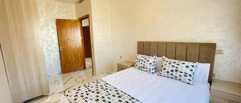 Un dormitorio con cama, mesitas de noche, un armario de madera y suelo de mármol.