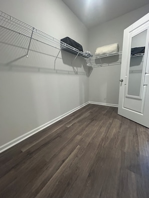 Een kamer met een houten vloer, witte wanden, een witte deur en een metalen schap met een zwart voorwerp erop.