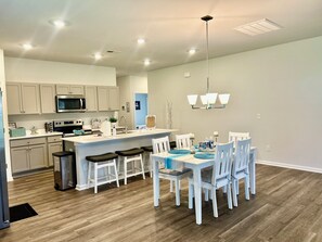 A modern kitchen with a central island, white cabinetry, and a dining area with a white table and chairs. - Southport Seascape~Family Coastal Getaway~Near Beaches & Waterfront Dining (Southport)