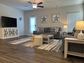 A living room with a grey sofa, a wooden coffee table, a TV on a cabinet, starfish wall art, and a ceiling fan. - Southport Seascape~Family-Friendly,Spacious, Near Beaches & Waterfront Dining (Southport)
