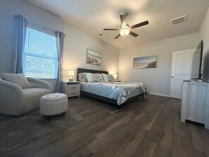A bedroom with a bed, nightstands, a chair, a ceiling fan, and artwork on the walls. - Southport Seascape~Family-Friendly,Spacious, Near Beaches & Waterfront Dining (Southport)