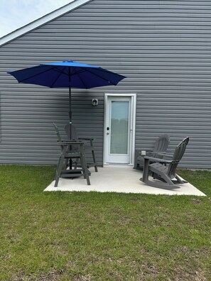 Een terras met twee Adirondack-stoelen, een tafel en een blauwe parasol.