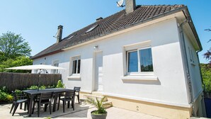 A white house with a tiled roof, a patio with a table and chairs, and a potted plant. - Vacation home in Normandy (Aure sur Mer)