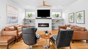 A modern living room with leather sofas, a black armchair, a TV, and a fireplace. - Talulah Sunrise (Panama City Beach)