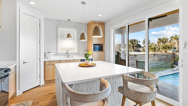 A modern kitchen with a large island, pendant lighting, and a view of a backyard with a pool. - Talulah Sunrise (Panama City Beach)