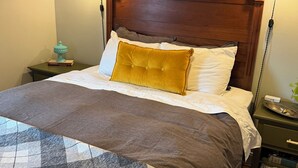 Una cama bien hecha con un cabecero marrón, una manta de cuadros y una almohada color mostaza.