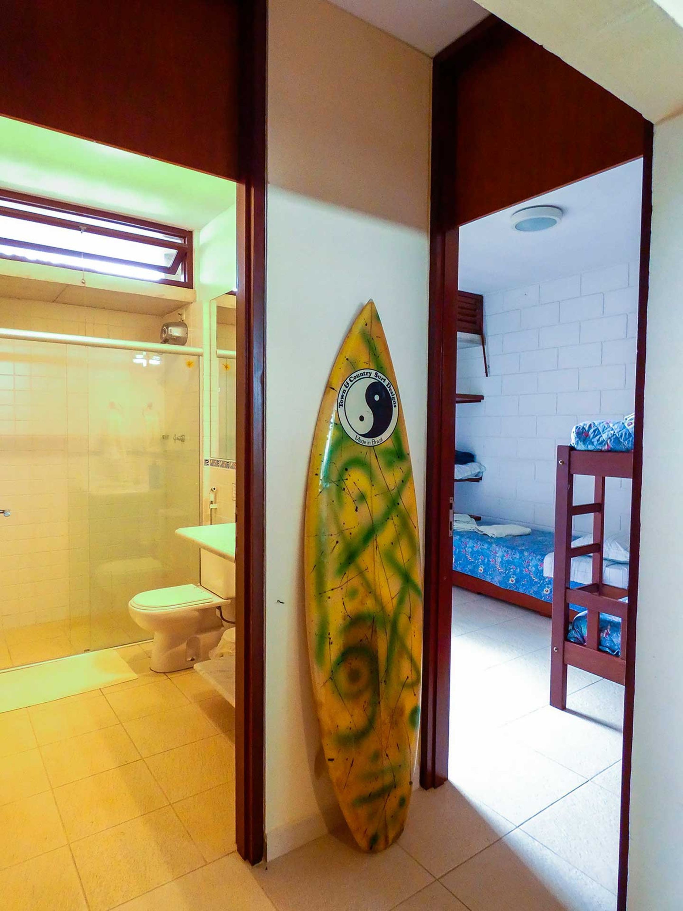 Un baño con ducha, inodoro y una tabla de surf apoyada en la pared.