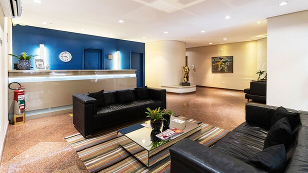A modern lobby with a reception desk, black leather sofas, a coffee table with magazines, and a fire extinguisher.