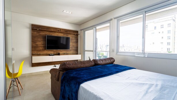 A modern bedroom with a large bed, a mounted TV, and a city view through the windows. - Apartamento com Wi-fi pr Ximo ao Metr Luz (São Paulo)