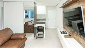 A modern living room with a brown leather sofa, a dining area with a table and chairs, a kitchen with white cabinets, and a large window. - Apartamento com Wi-fi pr Ximo ao Metr Luz (São Paulo)