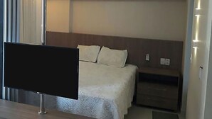 A hotel room with a bed, a bedside table, a flat-screen TV, and an air conditioning unit. - Apto Beira-mar com Wi-fi e Piscina em Fortaleza (Fortaleza)