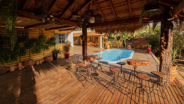 A wooden deck with a pool, surrounded by potted plants and metal chairs. - Pesqueiro - Rancho com Lazer Completo em Coxim MS (Coxim)