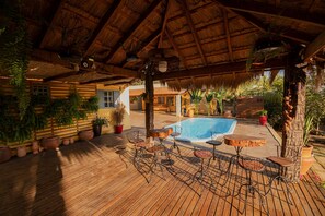 A wooden deck with a pool, surrounded by potted plants and metal chairs. - Pesqueiro - Rancho com Lazer Completo em Coxim MS (Coxim)