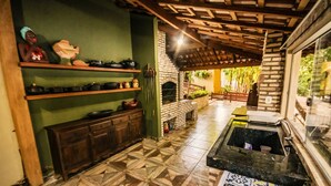 A kitchen with a brick oven, shelves with cookware, and a tiled floor. - Pesqueiro - Rancho com Lazer Completo em Coxim MS (Coxim)