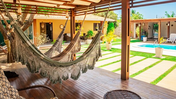 A hammock under a wooden pergola, a pool, and a patio area with potted plants. - Casa em Cond Fechado em Barra de Santo Ant nio AL (Barra de Santo Antonio)