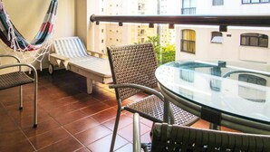 A balcony with a hammock, lounge chairs, and a glass-top table. - Timo Apto a 200m - Praia das Pitangueiras Guaruj (Guarujá)