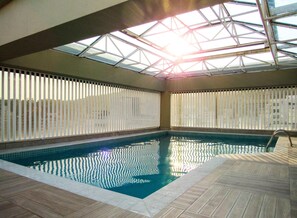 Ein Hallenbad mit Oberlichter, gefliesten Wänden und einer Holzterrasse.