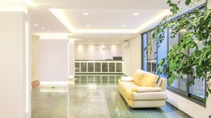 A modern interior with a sofa, a kitchen area, and a large window with a plant. - Timo Apto a 200m - Praia das Pitangueiras Guaruj (Guarujá)
