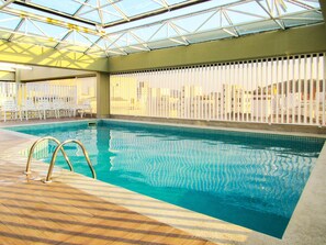 Ein Innenpool mit Glasdach, Holzboden und weißen Stühlen.