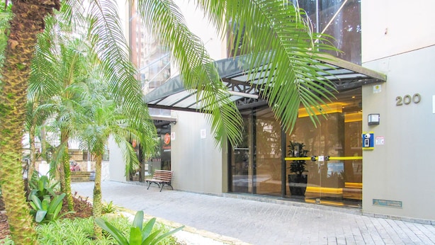 A modern building with a glass entrance, a bench outside, and a number '200' on the wall. - Timo Apto a 200m - Praia das Pitangueiras Guaruj (Guarujá)
