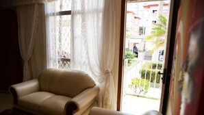 Ein Zimmer mit einem beigefarbenen Sofa, einem Holztisch und einem Fenster mit durchsichtigen Vorhängen.