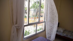 Ein Zimmer mit Bett, einem Vorhangfenster und Blick auf einen Spielplatz.