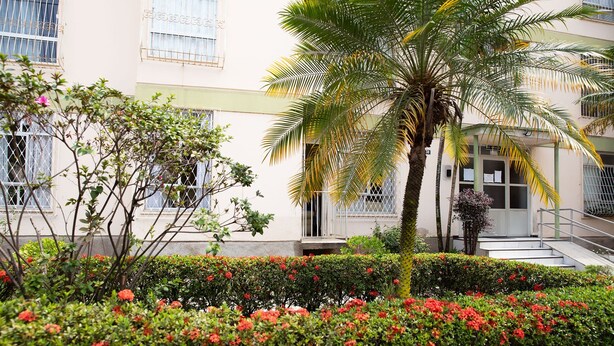 Ein Gebäude mit einem Balkon, einer Palme und roten Blumen im Garten.