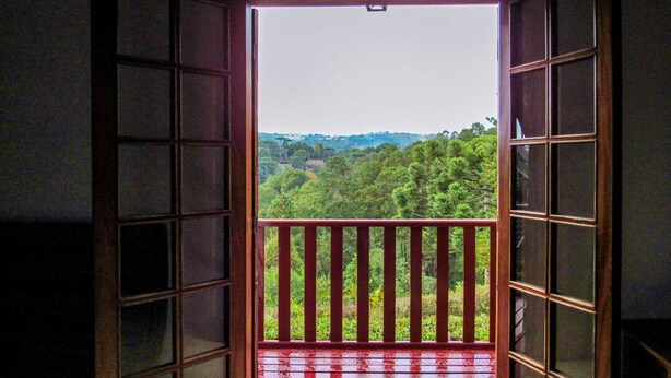 Une chambre avec vue sur un balcon et un paysage boisé.