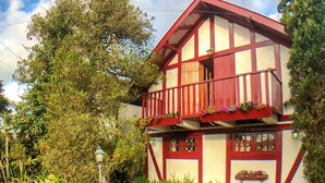 Une maison à deux étages dotée d’un balcon, entourée d’une végétation luxuriante et d’un jardin bien entretenu.
