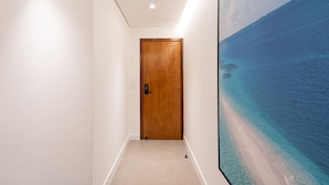 Un couloir avec une porte en bois et un grand tableau encadré représentant une plage.