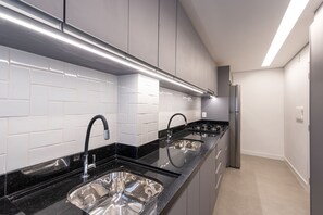 A modern kitchen with black countertops, stainless steel sinks, and a built-in oven.