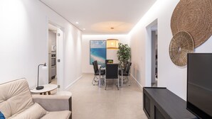 Un salon moderne comprenant un canapé, une table à manger avec des chaises, un téléviseur et un élément décoratif fixé au mur.