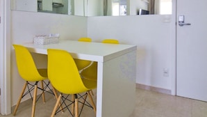 Un comedor pequeño con una mesa blanca y sillas amarillas, un espejo grande y una puerta con manija.