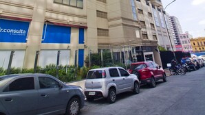 Un edificio alto con varios pisos, un escaparate azul en la planta baja y varios coches estacionados adelante.