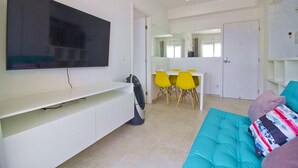 Una sala de estar moderna con un televisor de pantalla plana, un sofá color turquesa y una zona de comedor con sillas amarillas.