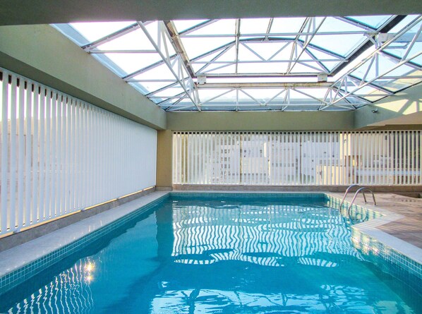 En indendørs swimmingpool med skydetag, flisebeklædte vægge og uhindret udsigt ud