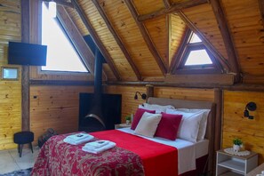 A wooden cabin bedroom with a bed, a television, and a fireplace.