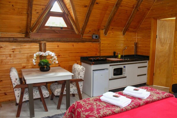 A cozy cabin with a wooden interior, a dining area with a table and chairs, a kitchenette, and a bed with neatly folded towels.